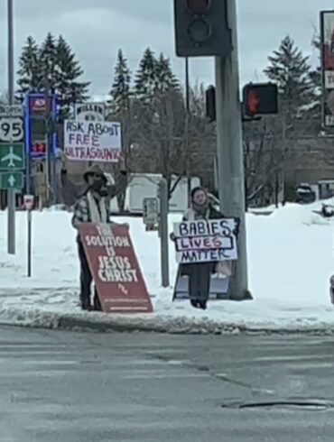 Protesters stand at the intersection of two busy roads