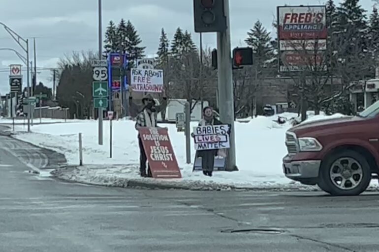 Protesters stand at the intersection of two busy roads